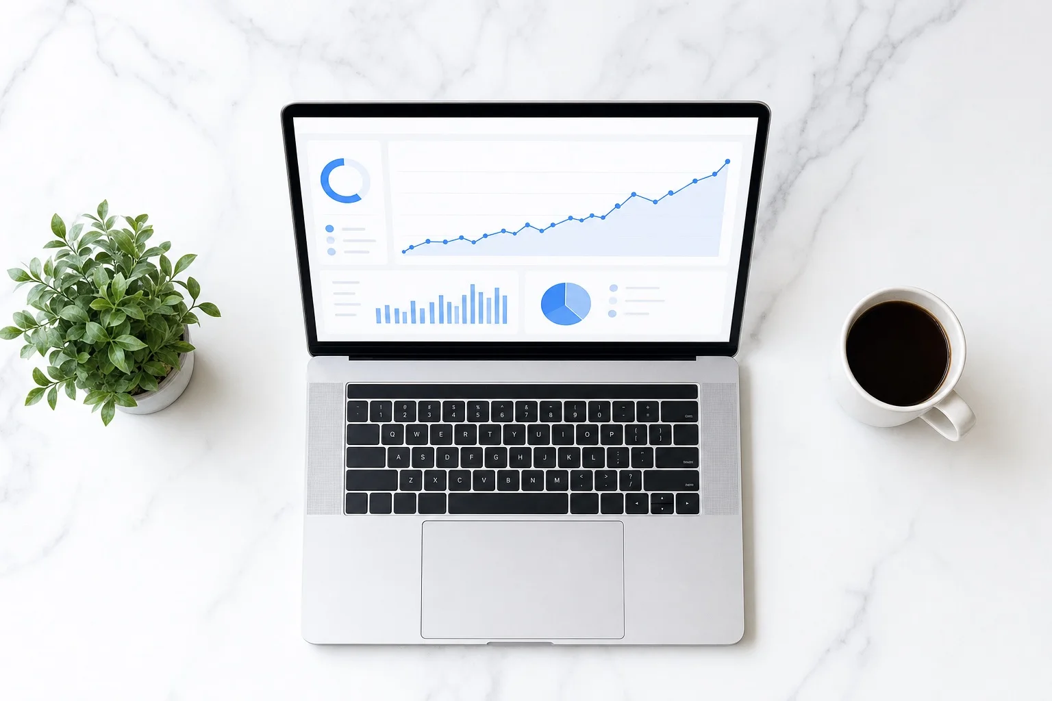 Top-down flat lay of laptop with revenue chart, coins, and coffee on marble